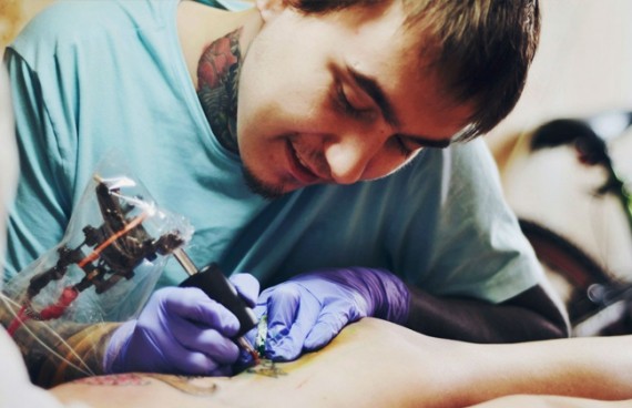Тату-мастер набивает татуировку на руке у клиента